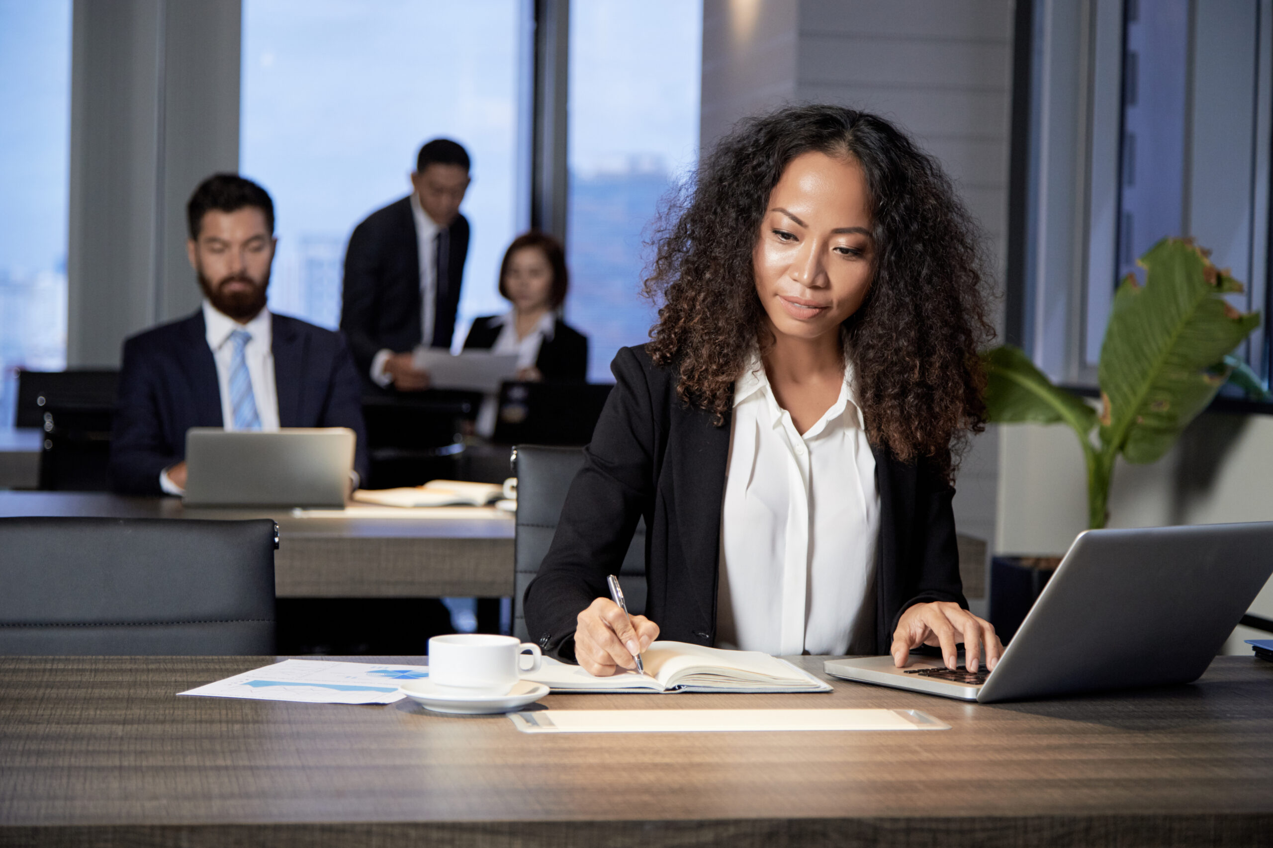 Woman writing on her notebook in front of her laptop inside an office 