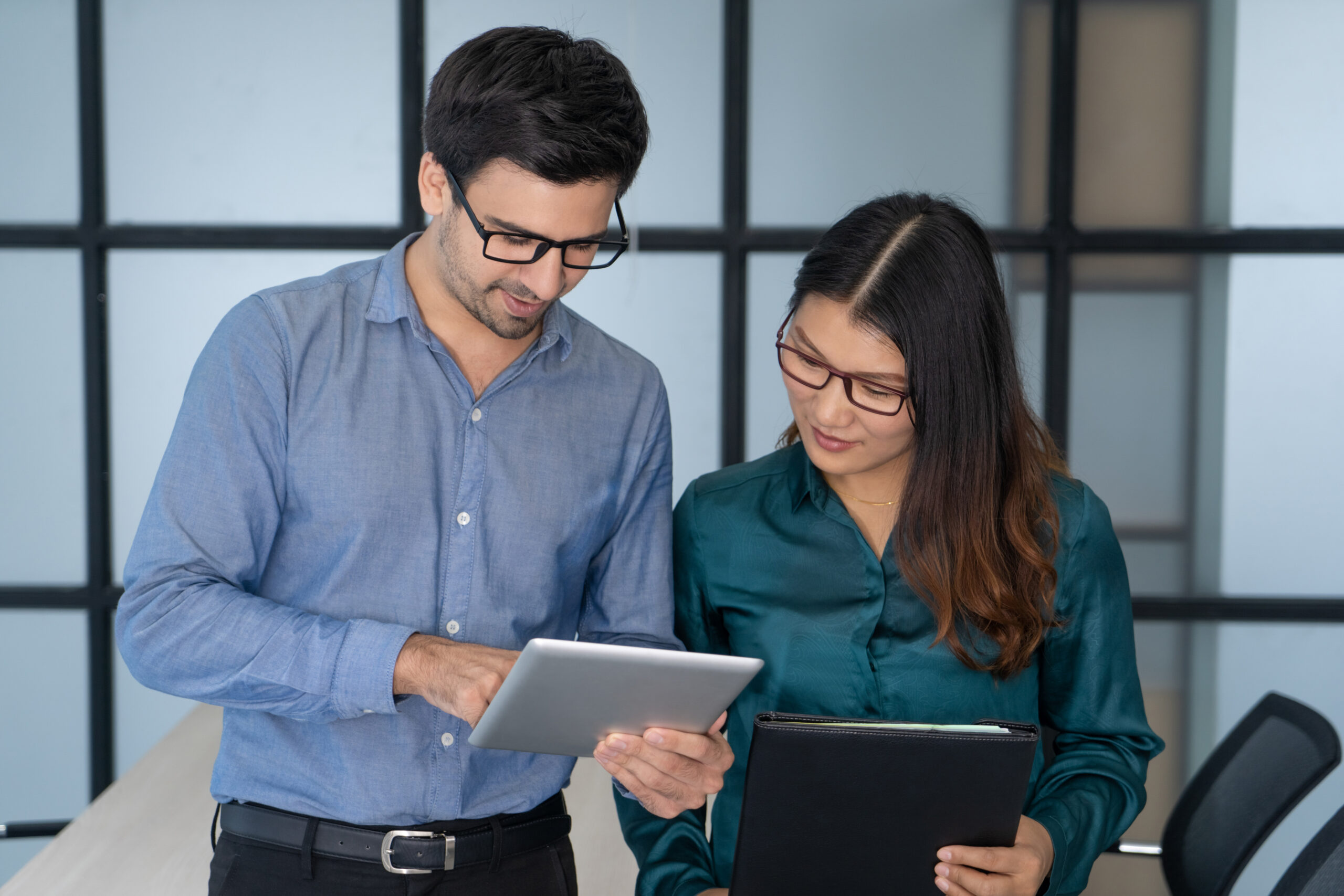 Two colleagues collaborating in an office, reviewing data on a tablet and discussing technology-driven solutions.