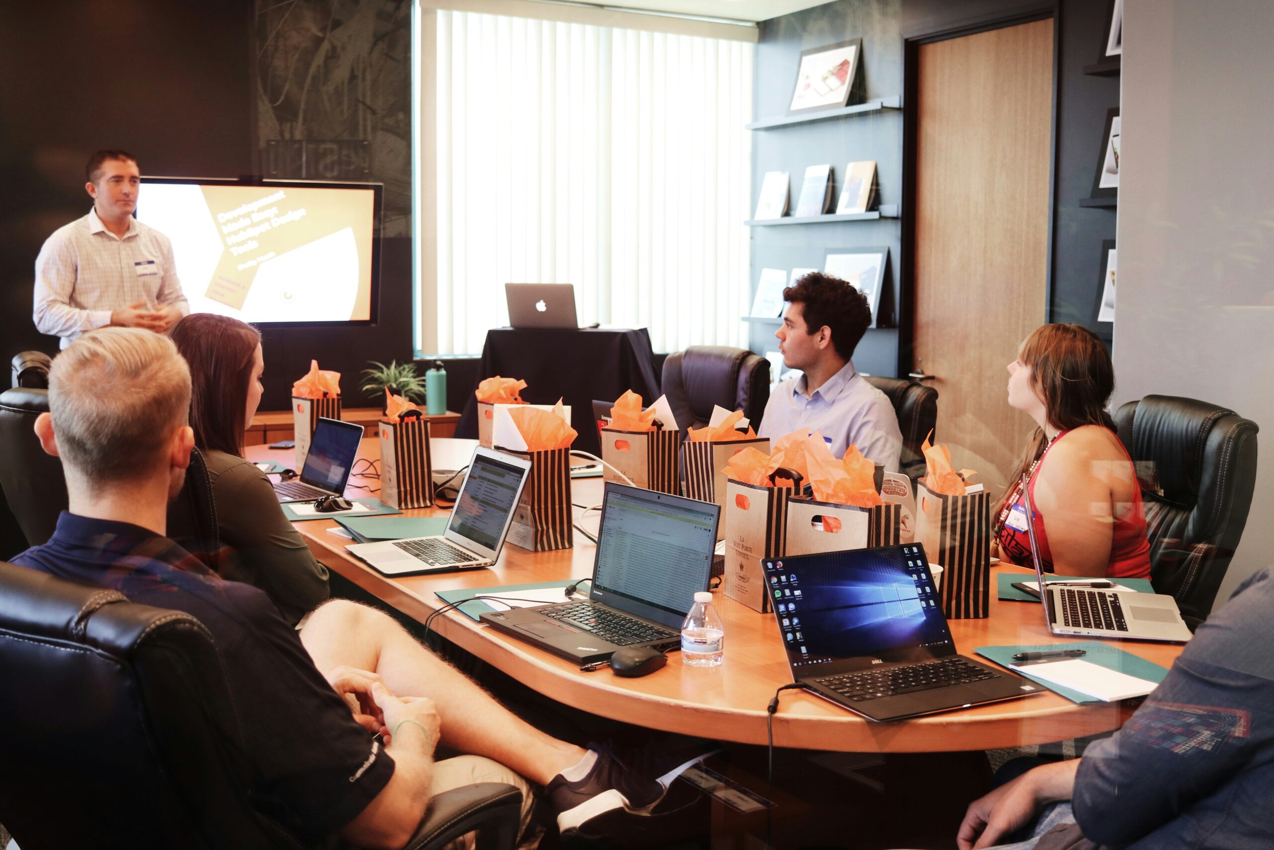 Team gathered in a conference room listening to a presentation with laptops on the table.